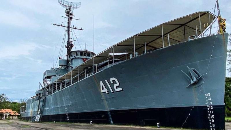 Серый корпус военного корабля с бортовым номером 412, стоящего на берегу в Паттайе. На палубе видны металлические конструкции, мачта с антеннами и навес, а на корме размечены ватерлинии с глубинами.