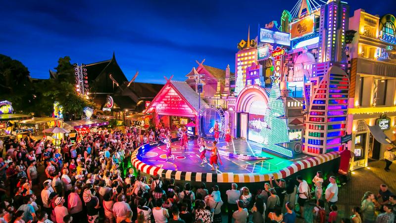 Уличная сцена Viva Bangkok в парке Phuket FantaSea: представление перед толпой зрителей среди неоновых фасадов