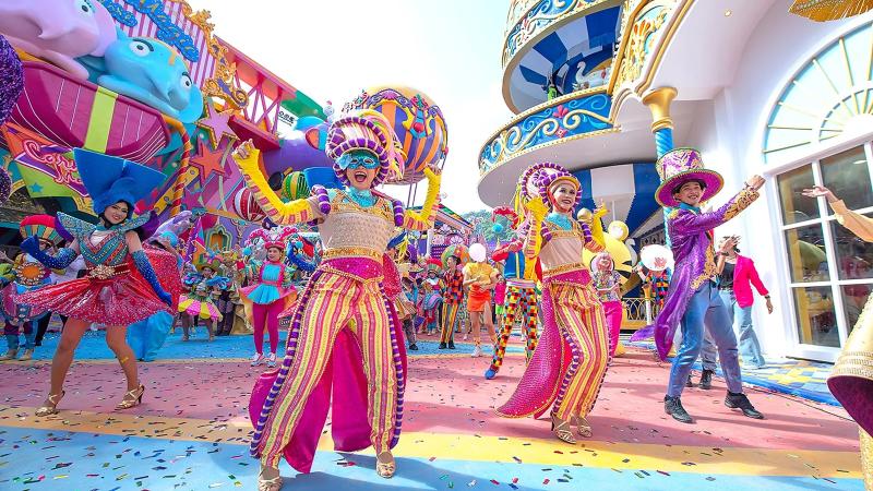 Артисты в полосатых костюмах танцуют среди гостей на улице парка Carnival Magic