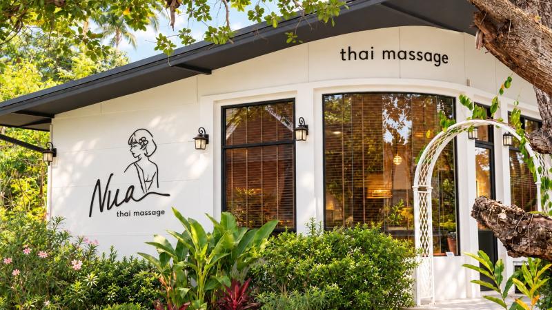 Белый дом спа-салона Nua Thai Massage в Раваи: логотип на стене, арка и сад у входа
