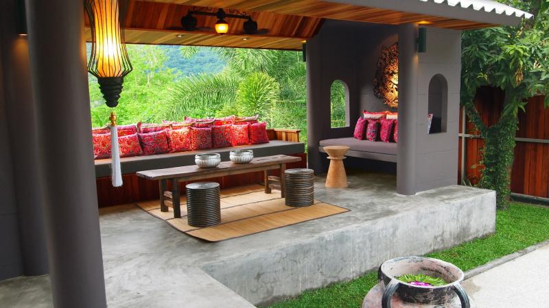 Беседка с красными подушками и низким столиком в саду салона Oasis Sky Breeze