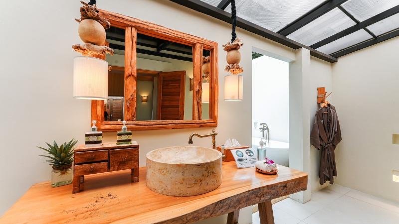 Раковина на деревянной столешнице и зеркало в ванной виллы салона Oasis Tropical Retreat