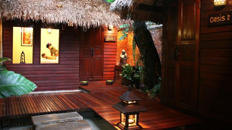 Деревянные виллы под соломенными крышами с табличками Oasis 1 и Oasis 2, в окне мастер делает массаж