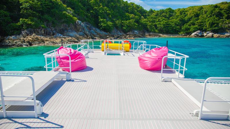 Верхняя палуба катамарана SeaStar с розовыми пуфами, впереди остров и бирюзовая вода