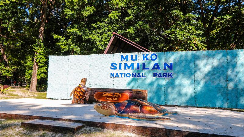 Стенд национального парка Му Ко Симилан на острове, перед ним фигура черепахи и табличка Similan
