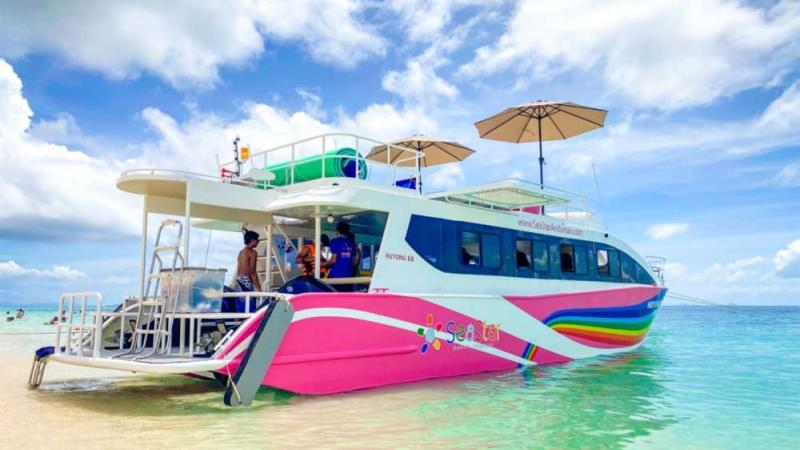 Двухпалубный скоростной катамаран SeaStar Huyong 88 с розовым корпусом у белого пляжа, наверху зонты