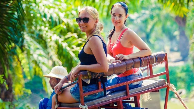 Две туристки в кресле на спине слона, внизу погонщик в панаме