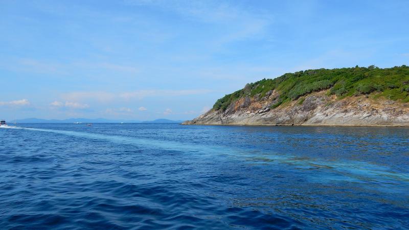 Скалистый берег острова Рача с моря, на синей воде — след катера