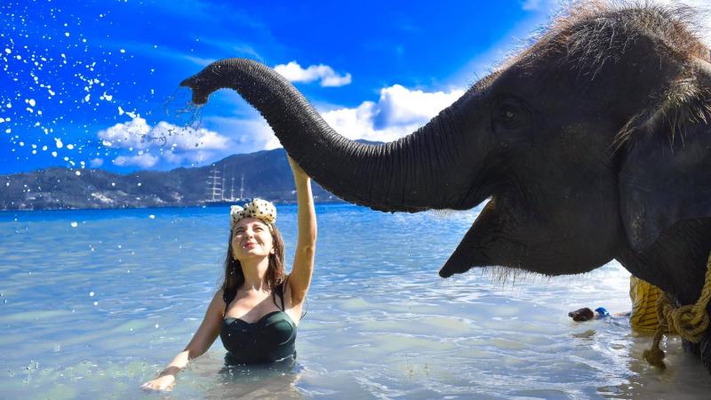 Слон поднял хобот над девушкой в море, брызги на фоне залива Патонг — Lucky Beach