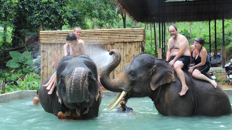Гости сидят на слонах в бассейне Kok Chang Safari, слон поливает их водой из хобота