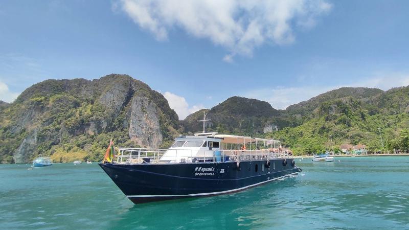 Паром Phi Phi Cruiser у зелёных холмов Пхи-Пхи, у берега — лодки-лонгтейлы