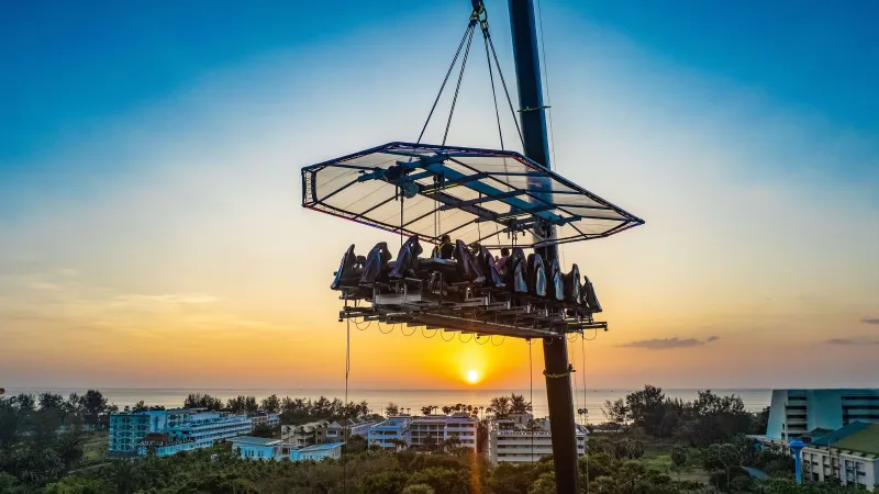 Платформа Dinner in the Sky с гостями на высоте 50 метров над Кароном на закате, солнце садится в море