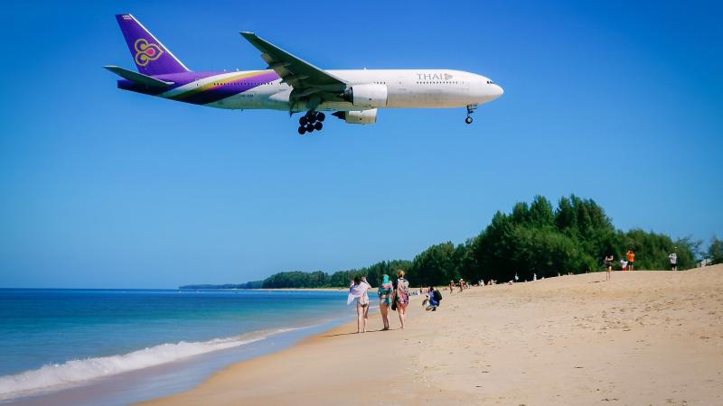 Самолёт Thai Airways низко над пляжем Май Кхао у аэропорта Пхукета, по песку гуляют туристы