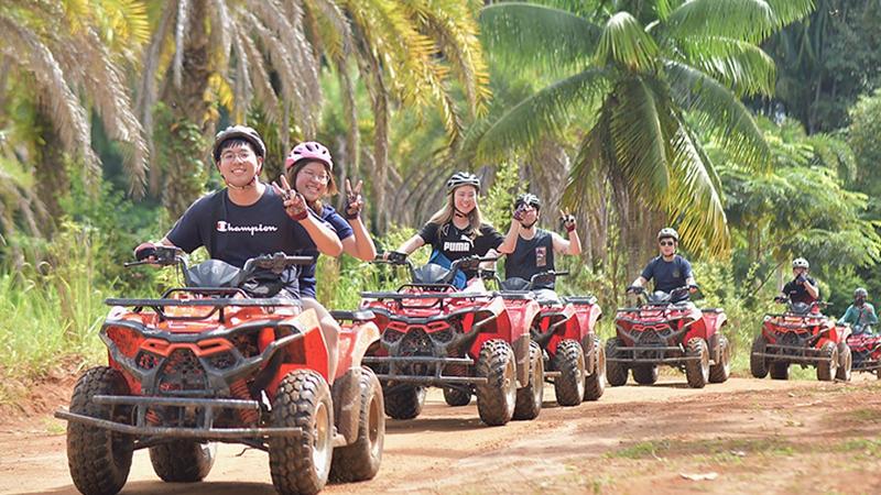 Колонна квадроциклов Phuket ATV Tour на грунтовой трассе среди пальм, гости машут в камеру