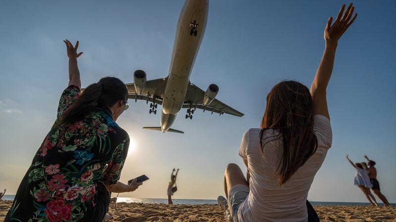 Туристки на пляже Май Кхао фотографируются с самолётом, который садится над головой