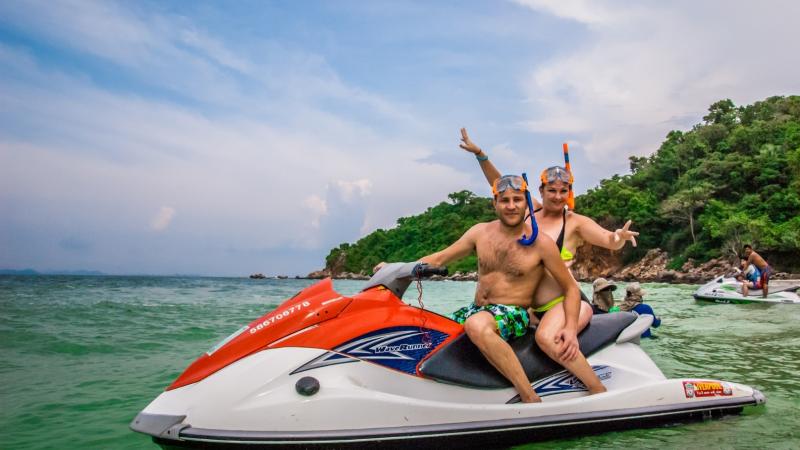 Два мужчины на водном мотоцикле в тропической бухте у берега с густой растительностью. Оба в масках для снорклинга, один машет рукой, на заднем плане виден второй катер с пассажирами.