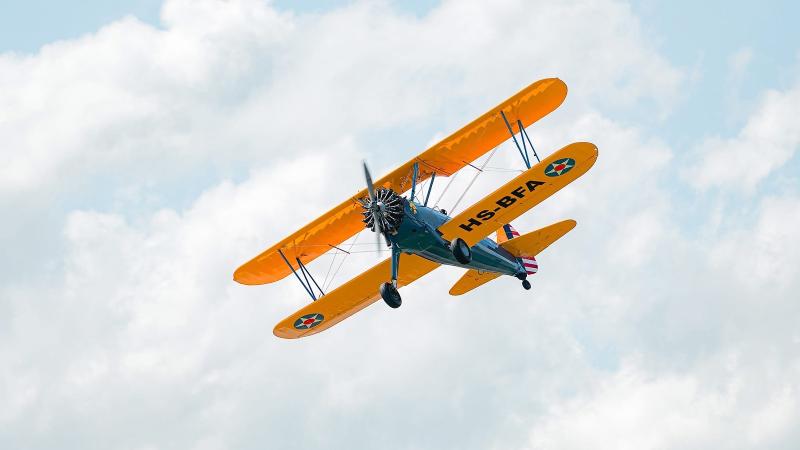 Оранжевый биплан Stearman в полёте среди облаков