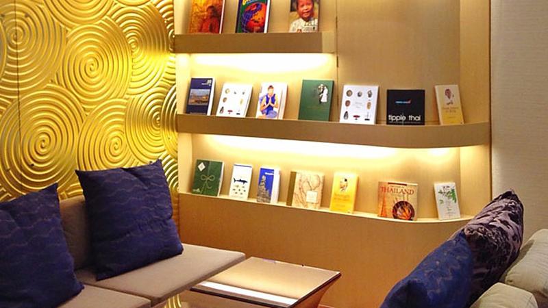 Уголок лаунжа: диван с подушками и подсвеченные полки с книгами о Таиланде