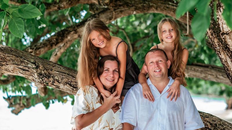 Родители и две дочки на ветвях большого дерева у пляжа — семейная фотосессия