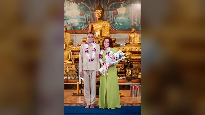 Жених и невеста в гирляндах из орхидей у статуи Будды — свадебное благословение в храме