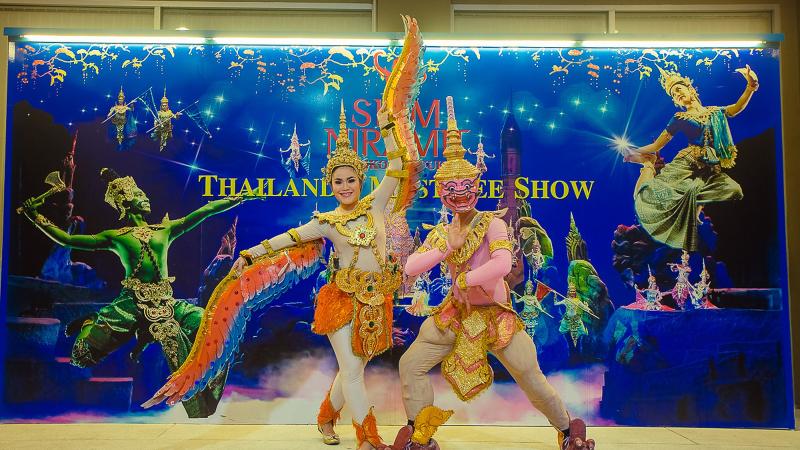 Артисты в костюмах тайского классического танца на фоне афиши Siam Niramit