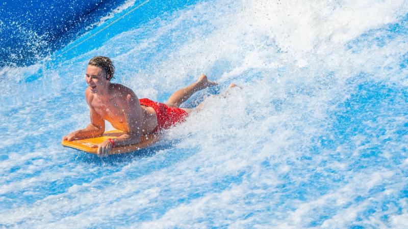 Гость катается лёжа на бодиборде по искусственной волне FlowRider в аквапарке Андаманда