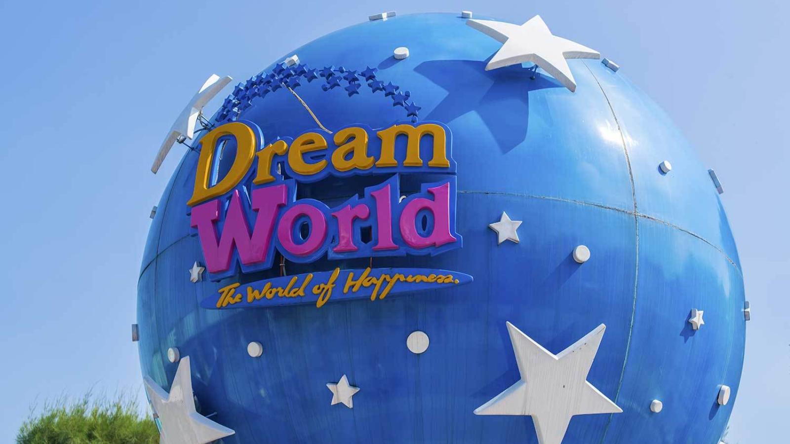 Большой синий сферический объект с белыми звёздами и надписью "Dream World - The World of Happiness" на фоне ясного голубого неба.