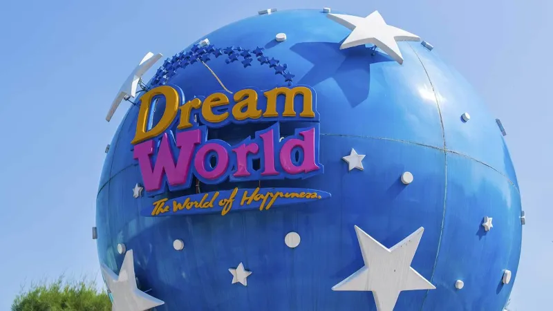 Большой синий сферический объект с белыми звёздами и надписью "Dream World - The World of Happiness" на фоне ясного голубого неба.